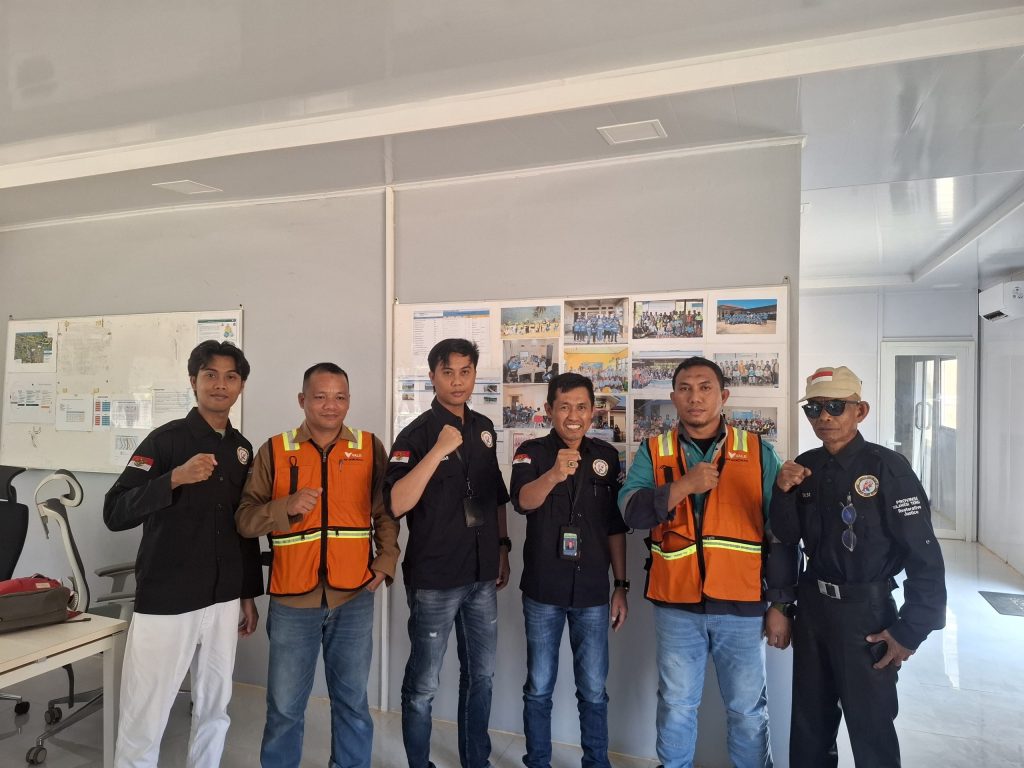 Sekelompok orang berfoto bersama di dalam ruangan, sebagian mengenakan rompi oranye dan pakaian berwarna gelap