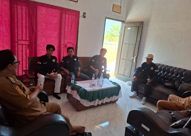 Sejumlah peserta duduk mengelilingi meja kecil dalam ruang pertemuan; beberapa berpakaian hitam dan seorang mengenakan seragam cokelat